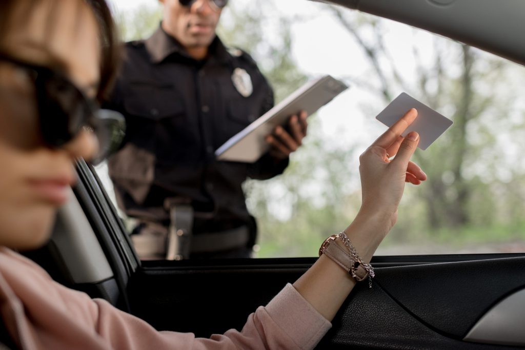 woman in sunglasses sitting in car and giving driver license to policeman